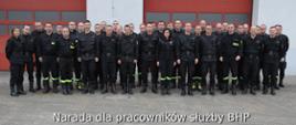 zdjęcie grupowe strażaków ubranychw czarne mundury dowódczo-sztanowe, w tle bramu garażowe 