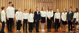 Grupa uczniów stoi na scenie w sali koncertowej.