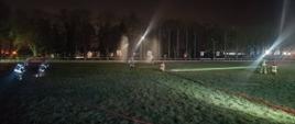 Nocne manewry taktyczne, na murawie stadionu ćwiczą zastępy strażaków, przy każdym zastępie widoczna doprowadzona linia wodna