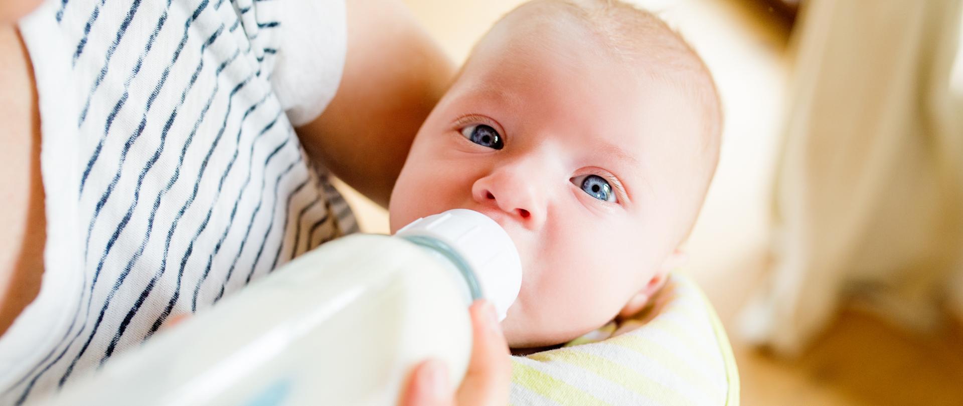 Close up of unrecognizable mother holding her baby son in the arms, feeding him with milk from bottle
