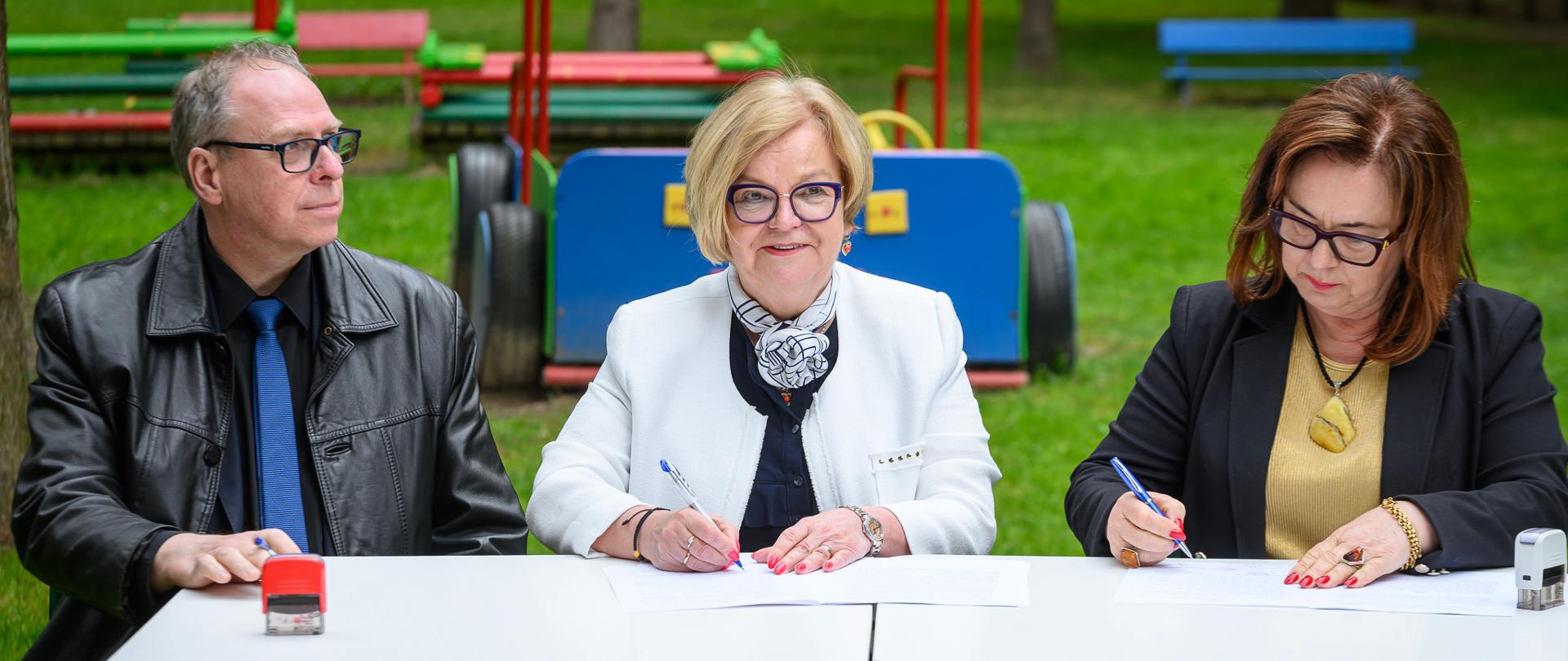 Zdjęcie przedstawia trzy osoby podpisujące umowę