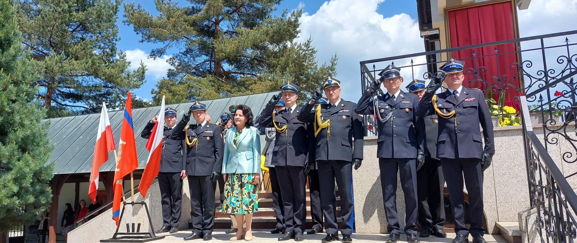 Na schodach przed kościołem stoją strażacy ubrani w mundury wyjściowe oddając honory. 