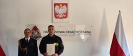 Zastępca Komendanta Powiatowego Państwowej Straży Pożarnej w Człuchowie bryg. Marcin Owczarski po przyjęciu ślubowania ze str. Mateuszem Żyła. W tle godło, flagi państwowe i logo PSP.