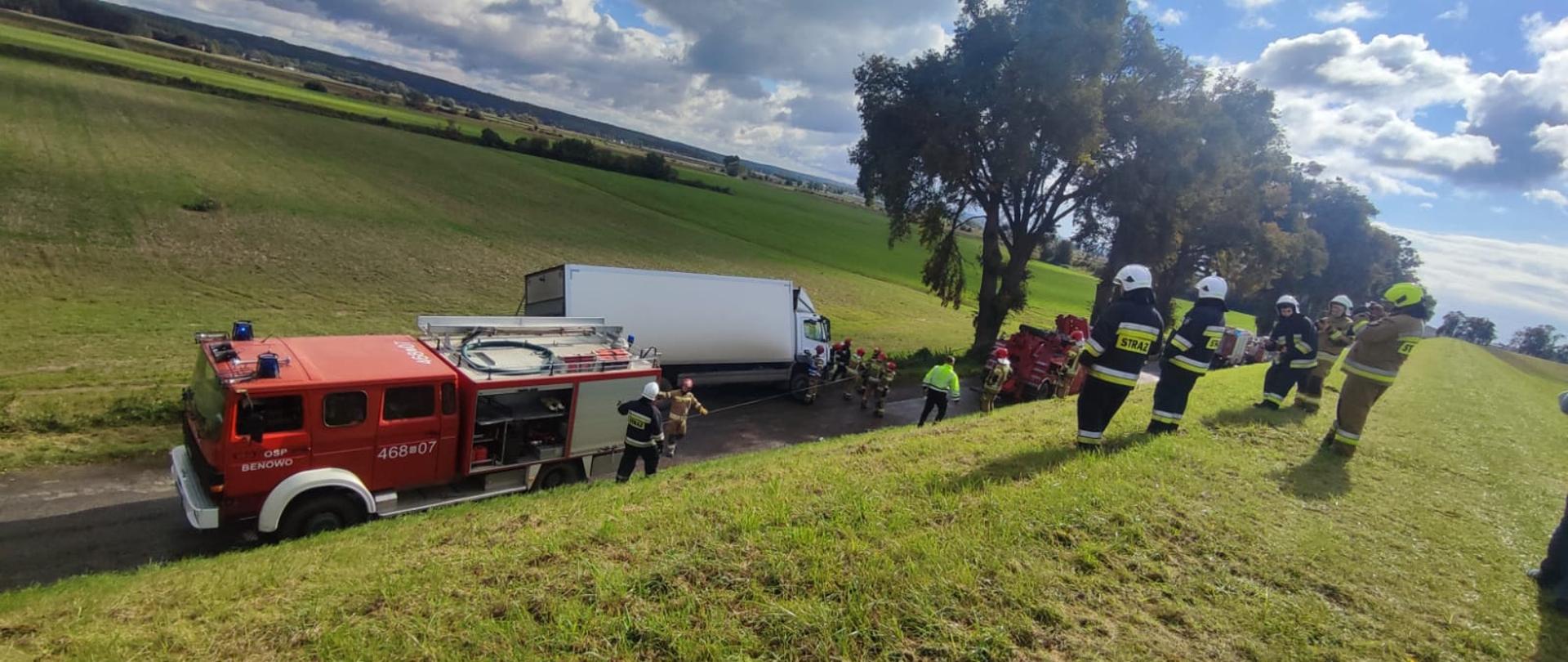 Samochód ciężarowy zagrożony przewróceniem oraz pojazdy ratownicze i strażacy stoją na jezdni