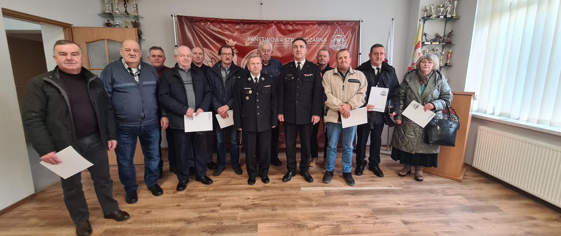 Strażacy i komendanci na zdjęciu grupowym na świetlicy