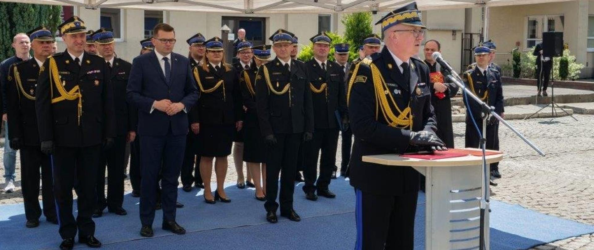 Zastępca komendanta głównego PSP podczas przemówienia. W tle zebrani goście pod namiotem