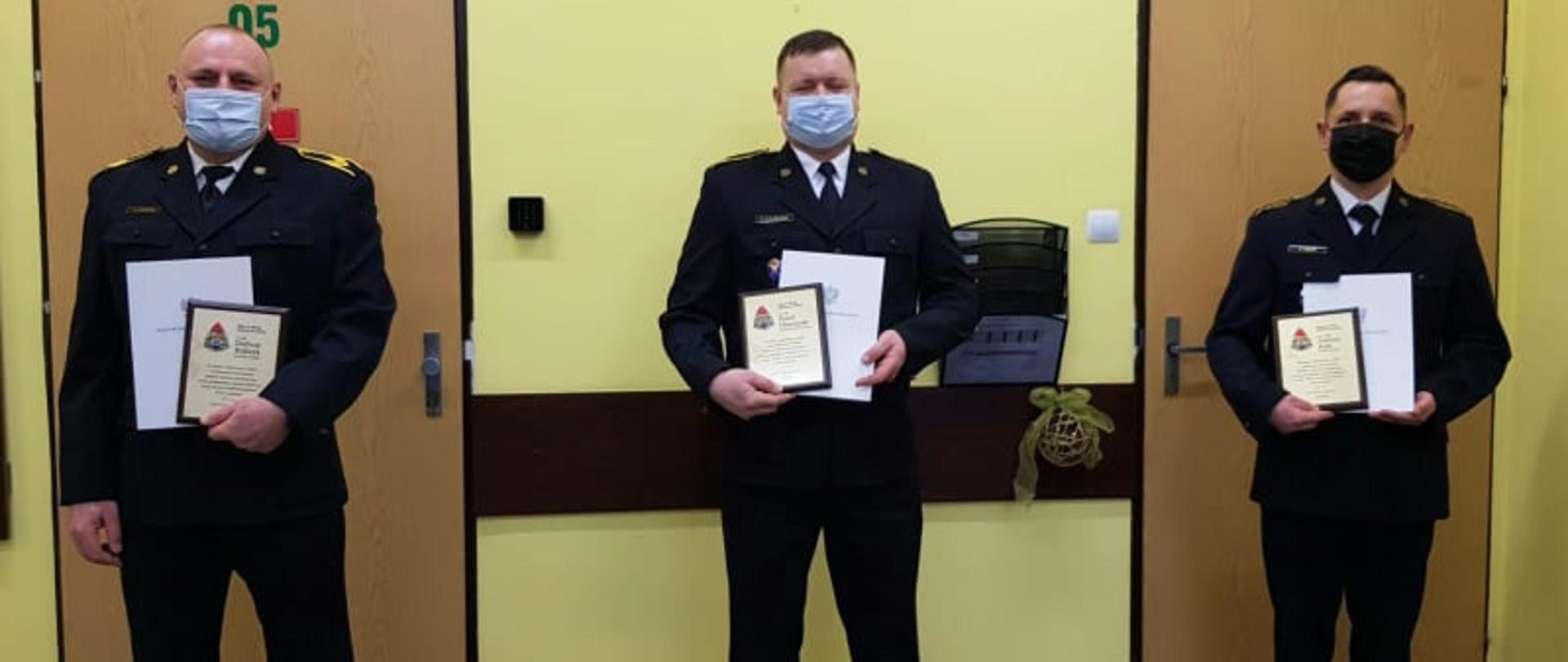 Trzech funkcjonariuszy odchodzących na zaopatrzenie emerytalne z wręczonymi listami gratulacyjnymi.