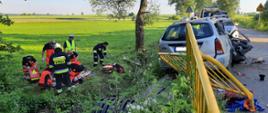 Rozbity samochód osobowy. Po lewej służby ratownicze udzielają pomocy osobie poszkodowanej.