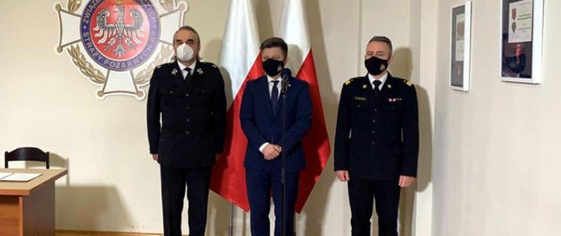 Kolorowe zdjęcie wykonane w jasnym pomieszczeniu. Od prawej stoją: w mundurze nadbryg. Andrzej Bartkowiak komendant główny PSP, pośrodku w ubraniu cywilnym Michał Dworczyk, szef Kancelarii Prezesa Rady Ministrów, po lewej w mundurze dh. Waldemar Pawlak, prezes ZG ZOSP RP. W tle na białej ścianie, z lewej strony, widoczny kolorowy znak Związku Ochotniczych Straży Pożarnych Rzeczypospolitej Polskiej, na środku dwie pionowo stojące flagi biało-czerwone, po prawej widoczne obrazy w ramach.