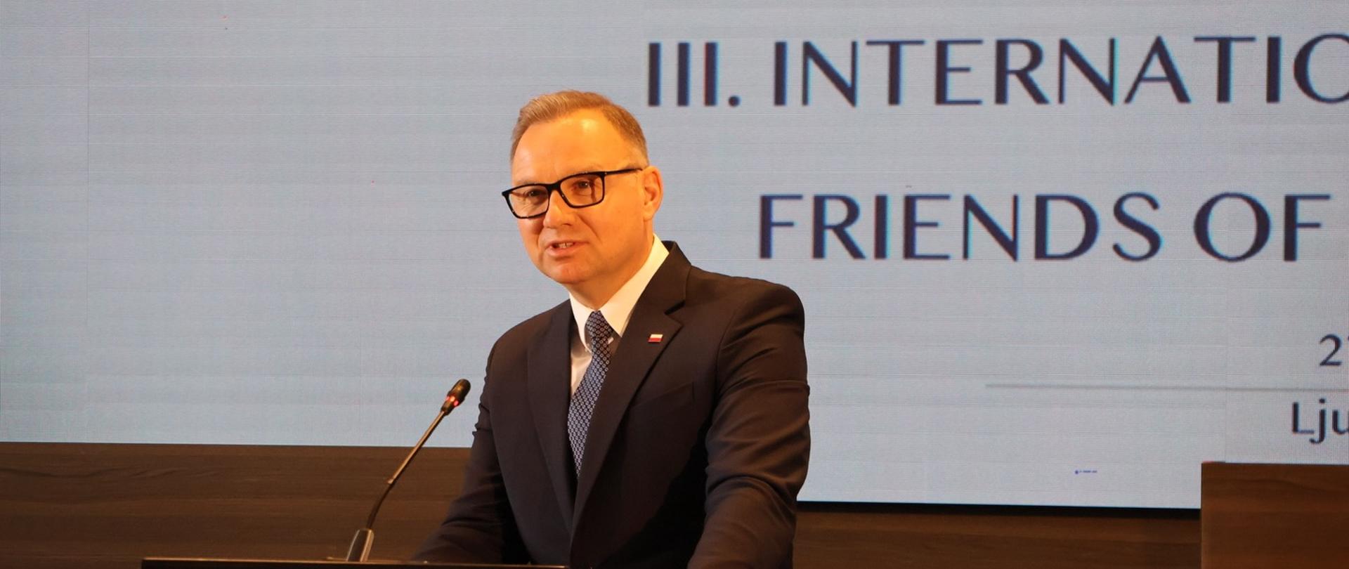 Mężczyzna w garniturze - A.Duda - przemawia przy mównicy podczas konferencji. W tle widoczny ekran z napisem dotyczącym konferencji „Friends of the Western Balkans”.
