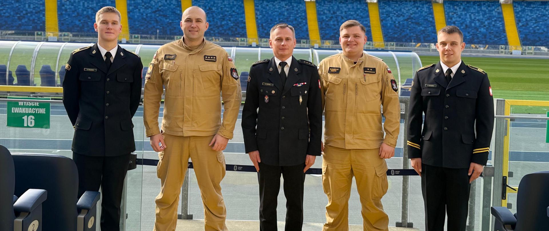 Pamiątkowe zdjęcie Zastępcy Komendanta Centralnej Szkoły PSP w towarzystwie czterech funkcjonariuszy Szkoły na tle murawy oraz trybun Stadionu Śląskiego