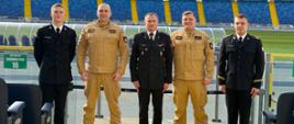 Pamiątkowe zdjęcie Zastępcy Komendanta Centralnej Szkoły PSP w towarzystwie czterech funkcjonariuszy Szkoły na tle murawy oraz trybun Stadionu Śląskiego