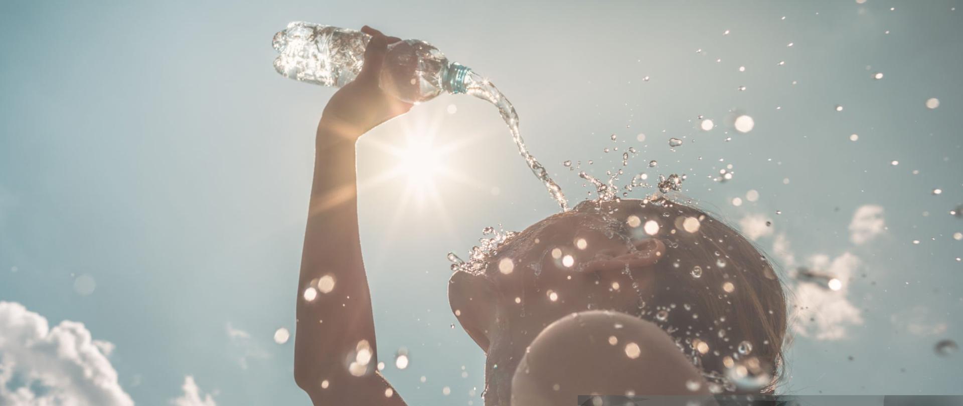 Woman cooling down splashing herself with bottle of water on a hot sunny day.