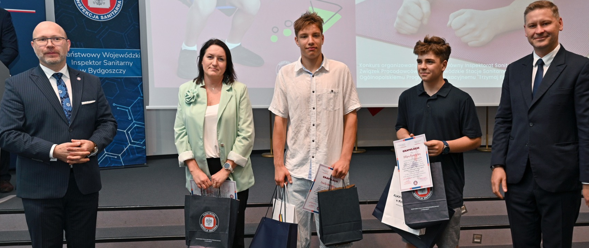 Wicewojewoda Kujawsko-Pomorski Michał Koniuch oraz Państwowy Wojewódzki Inspektor Sanitarny w Bydgoszczy wręczają podziękowania i nagrody Filipowi Burzychowi i Emilowi Witmanowi ze Szkoły Podstawowej nr 30 im. Szarych Szeregów z Oddziałami Dwujęzycznymi w Bydgoszczy.
