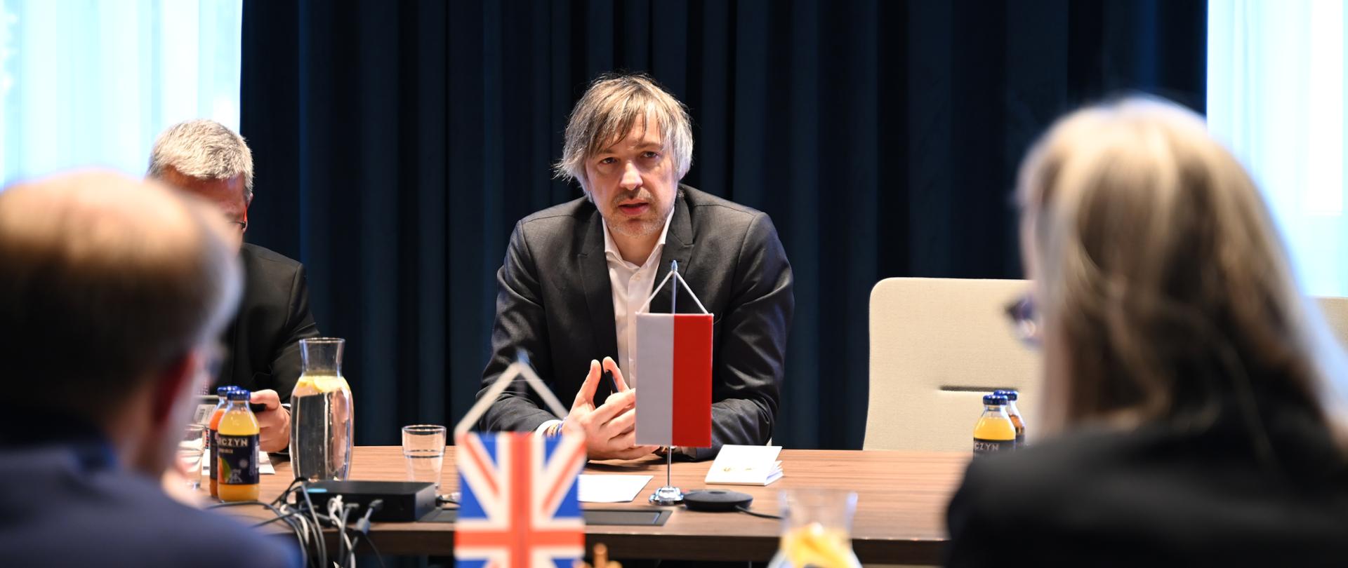 Wiceminister klimatu i środowiska Krzysztof Bolesta podczas spotkania z Michaelem Shanks’em, brytyjskim ministrem ds. energii. Wiceminister siedzi przy stole i prowadzi rozmowę.