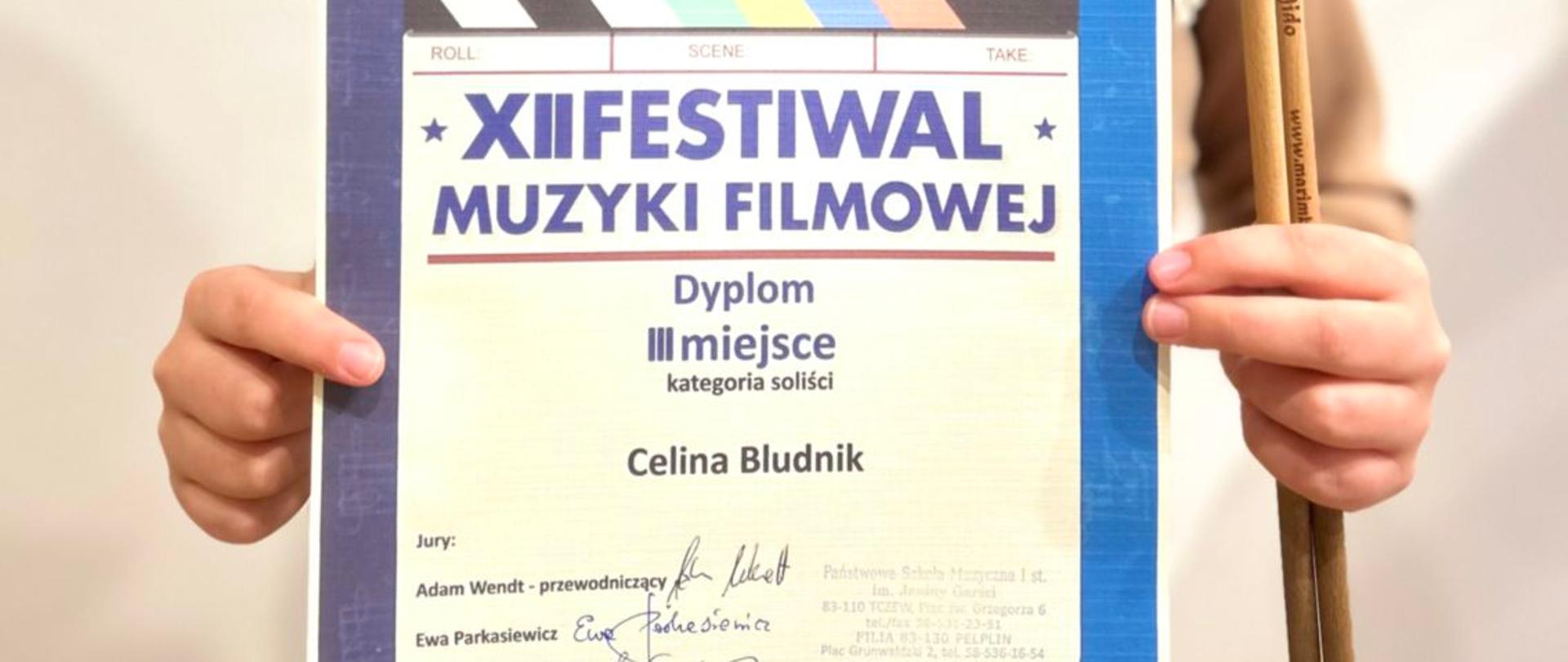 Zdjęcie przedstawia uczennicę klasy perkusji trzymającą dyplom za zdobycie dyplomu III miejsca na konkursie muzyki filmowej.