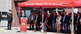 Na tle budynku Sekretarz Miasta Pan Mirosław Luks w trakcie przemówienia. Z prawej strony widoczni goście pod czerwonym namiotem. 
