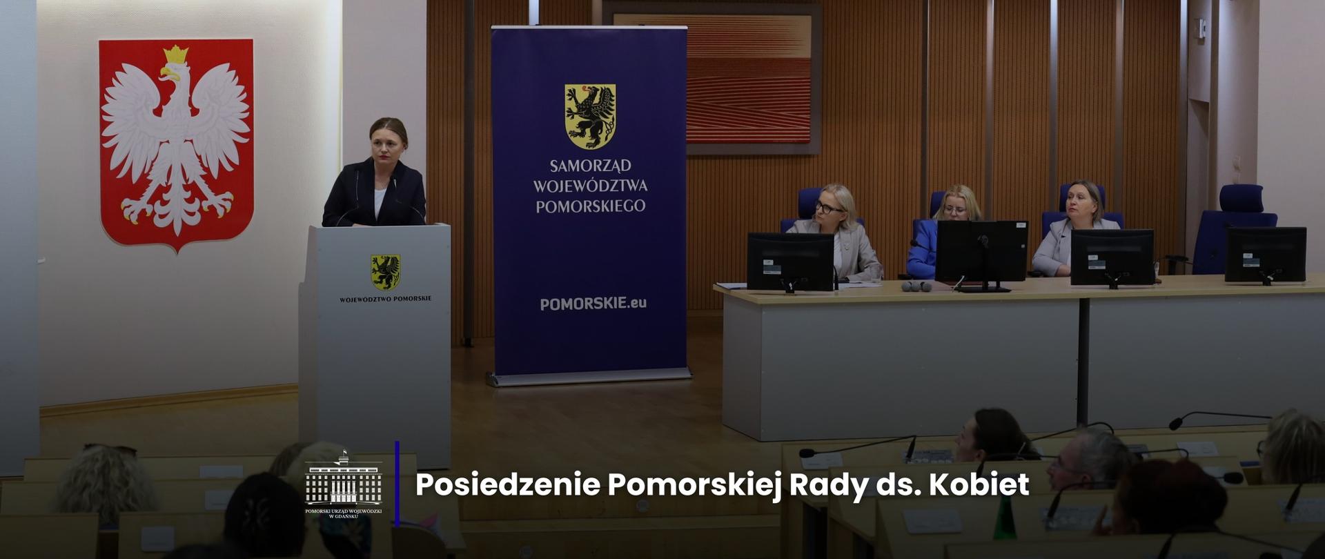 kobieta stoi na mównicy i przemawia, za nią godło Polski