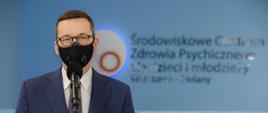 Premier Mateusz Morawiecki stoi przy mikrofonie podczas konferencji. W tle podświetlony napis na ścianie "Środowiskowe Centrum Zdrowia Psychicznego dla dzieci i młodzieży".