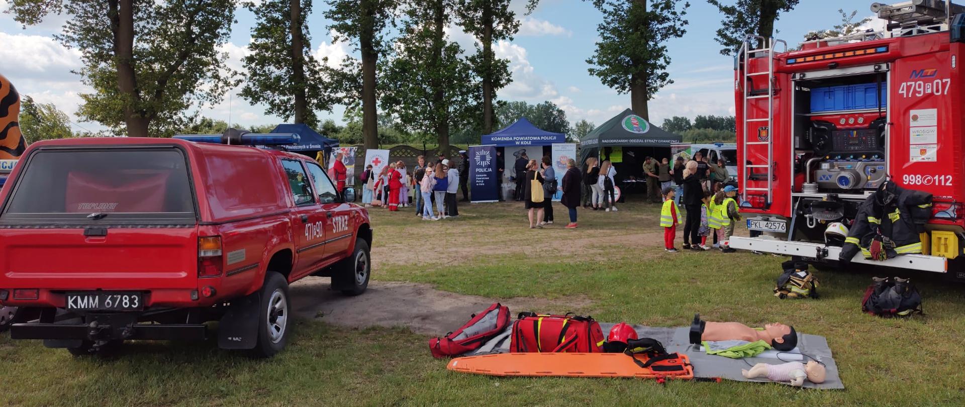 Zdjęcie przedstawia sprzęt do nauki udzielania pierwszej pomocy oraz dwa samochody straży pożarnej