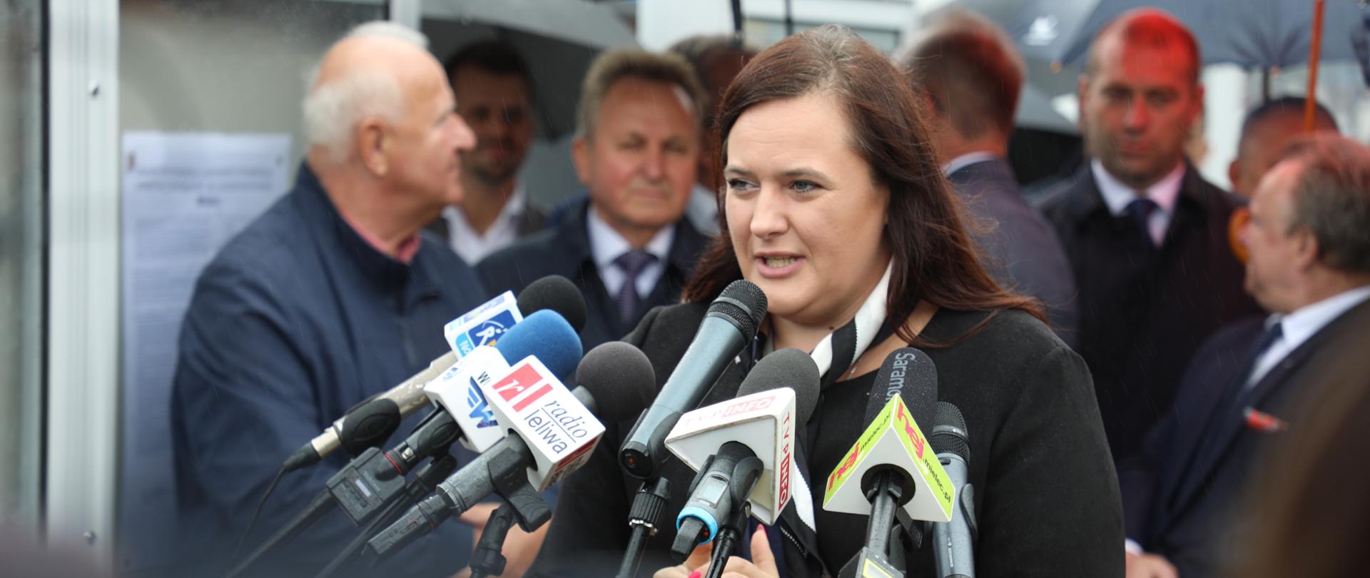 wiceminister Małgorzata Jarosińska-Jedynak mówi do mikrofonów, za nią pozostali uczestnicy uroczystości