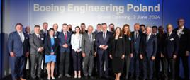 Zdjęcie zbiorowe, pod niebieską ścianą z napisem Boeing Engineering Poland stoi duża grupa osób.