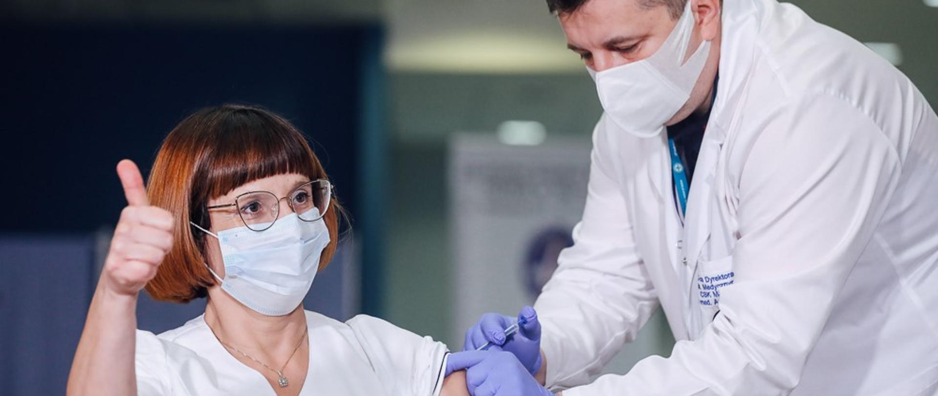 Pielęgniarka podczas szczepienia pokazuje kciuk uniesiony do góry.