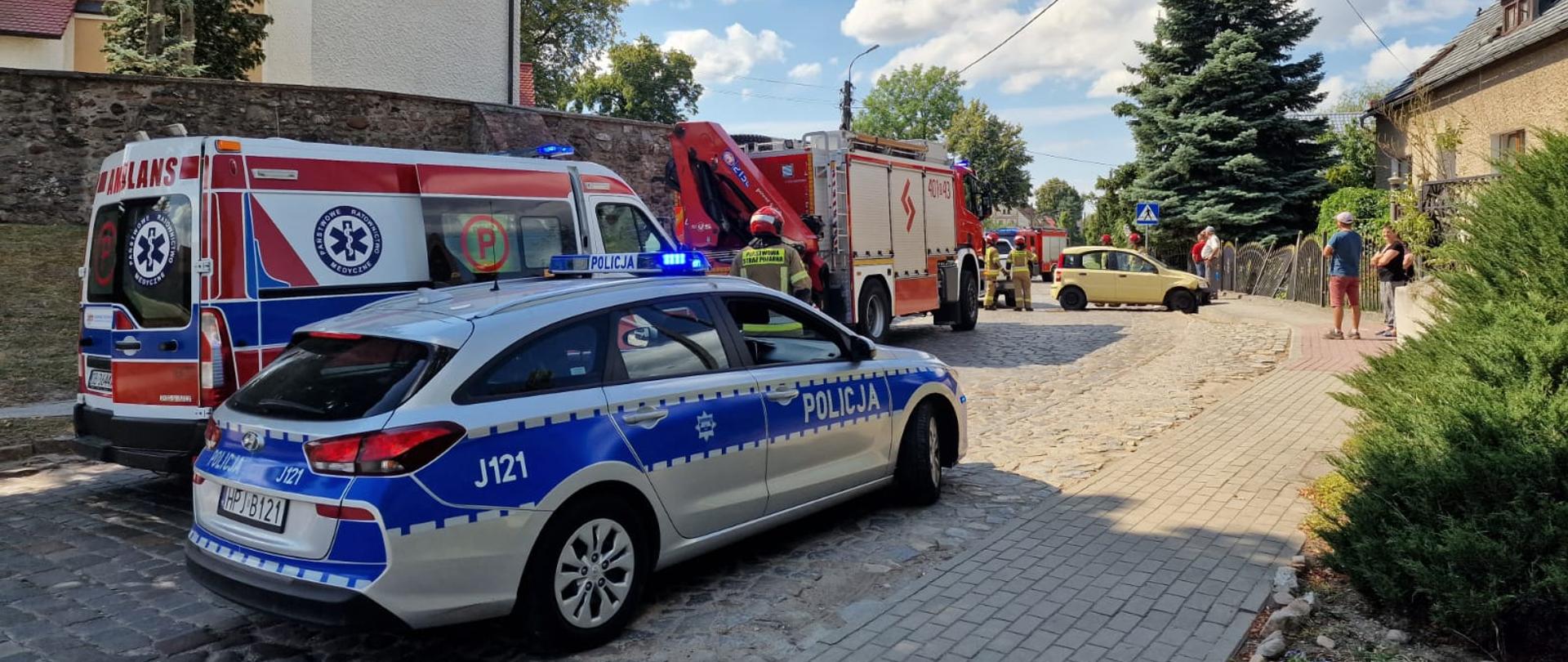 Wypadek z udziałem samochodu osobowego w miejscowości Pępice - zdjęcie przedstawia samochody służb (ZRM, policja i straż pożarna) w tle widać samochód koloru żółtego, który uległ wypadkowi