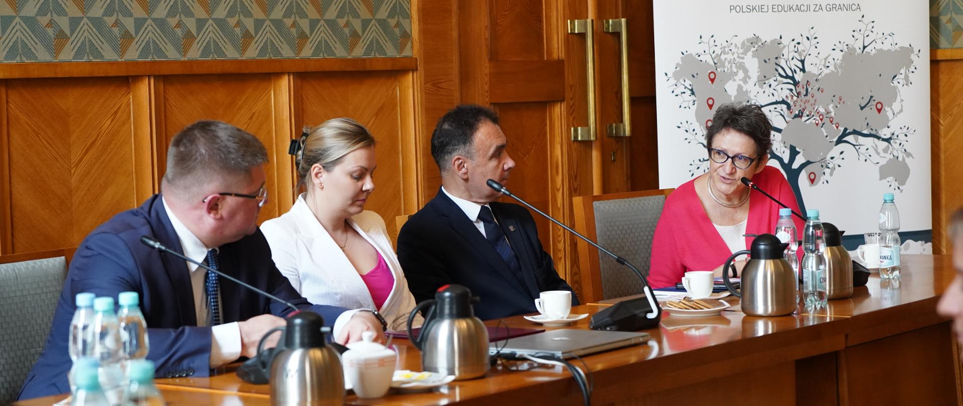 Za drewnianym stołem siedzi wiceminister Rzymkowski i kilka osób, za nimi pod ścianą baner z napisem ORPEG.