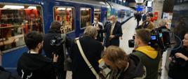 Wiceminister Waldemar Buda peronem przechodzi obok pociągu Connecting Europe Express, dziennikarze aparatami robią zdjęcia i kamerami filmują to przejście