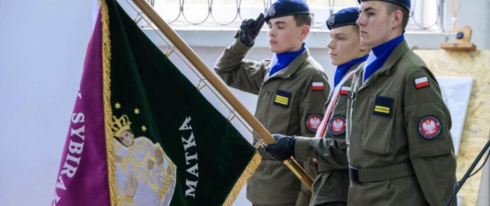 Zdjęcie przedstawia trzy osoby i sztandar Sybiraków