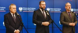 Minister funduszy i polityki regionalnej Grzegorz Puda, minister kultury i dziedzictwa narodowego Piotr Gliński oraz minister zdrowia Adam Niedzielski na konferencji prasowej podczas podpisania porozumień w sprawie realizacji wybranych zadań z programu Fundusze Europejskie na Infrastrukturę, Klimat, Środowisko 2021–2027, ministrowie stoją przy mikrofonach, za ich plecami telebim z logo MFiPR