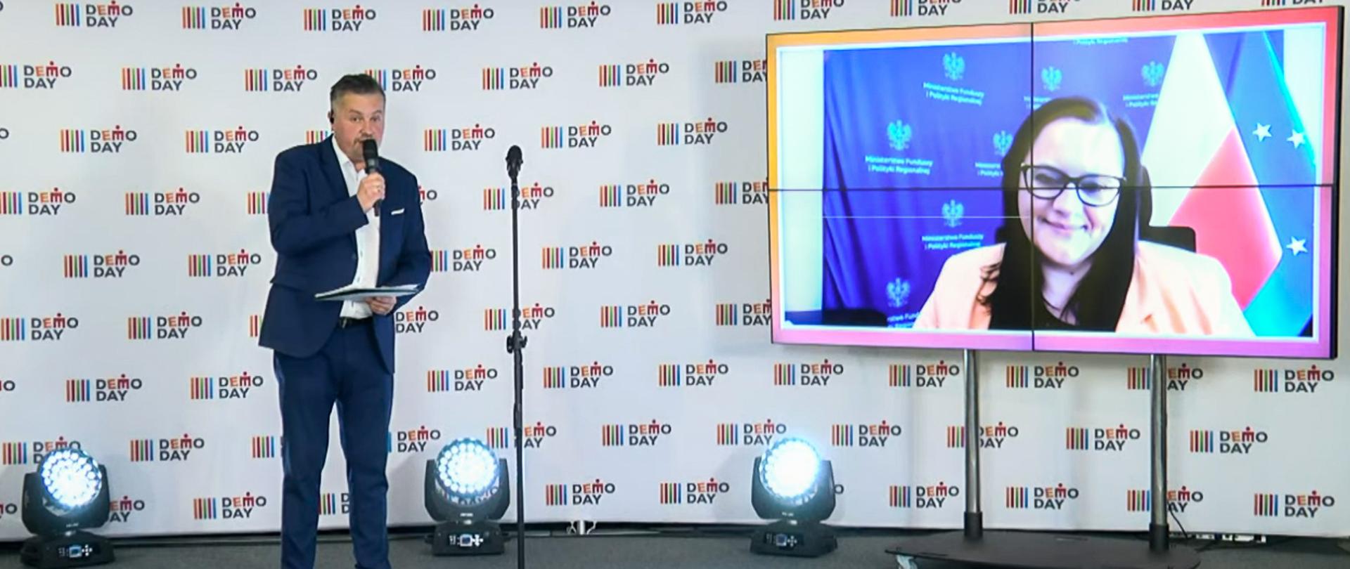 Na scenie mężczyzna z mikrofonem. Obok na ekranie twarz wiceminister Małgorzaty Jarosińskiej-Jedynak.