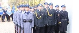 Strażacy oraz policjanci stoją obok siebie za nimi ustawione są poczty sztandarowe z jednostek organizacyjnych Państwowej straży Pożarnej.