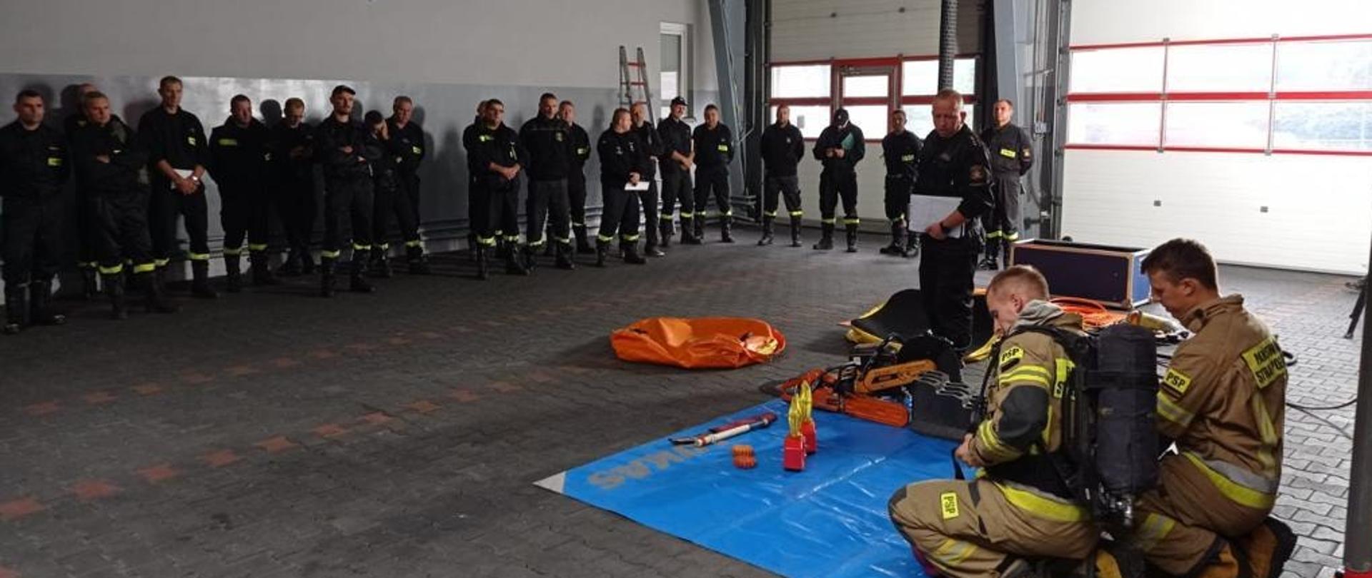 Na zdjęciu osoby przeprowadzające Szkolenie z zakresu bezpieczeństwa i higieny pracy w umundurowaniu bojowym oraz druhowie OSP podczas szkolenia praktycznego na garażu. 
