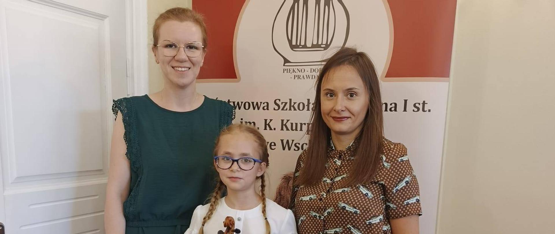 Uczennica trzymająca skrzypce oraz dyplom, w towarzystwie nauczycielek.