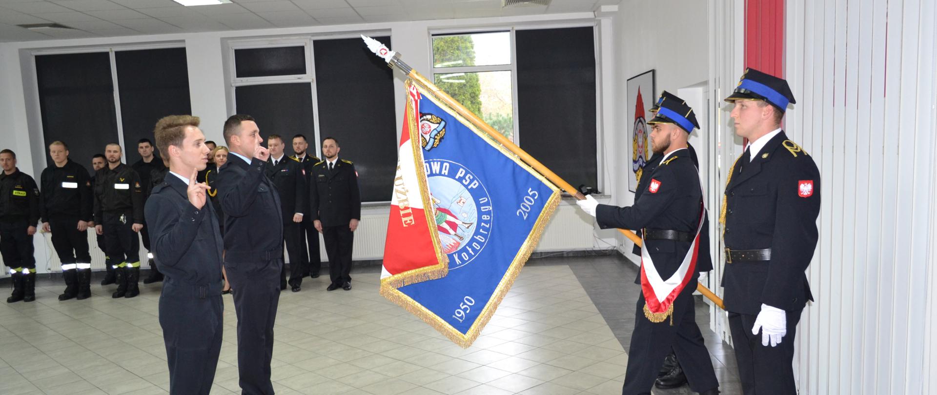 Dwaj strażacy składają ślubowanie na sztandar komendy, w tle grupa strażaków stojąca w rzędzie