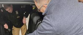pracownik salonu samochodowego Kia pokazuje zespół akumulatorów znajdujący się pod kanapą pasażera dwóm strażakom 