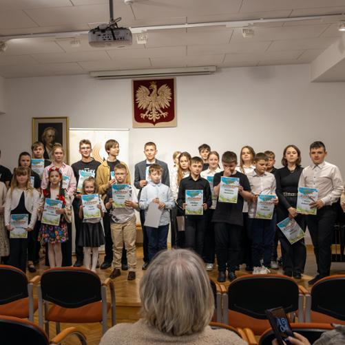 Uczestnicy szkolnego konkursu na scenie szkoły muzycznej, wszyscy trzymają w rękach dyplomy uczestnictwa. 