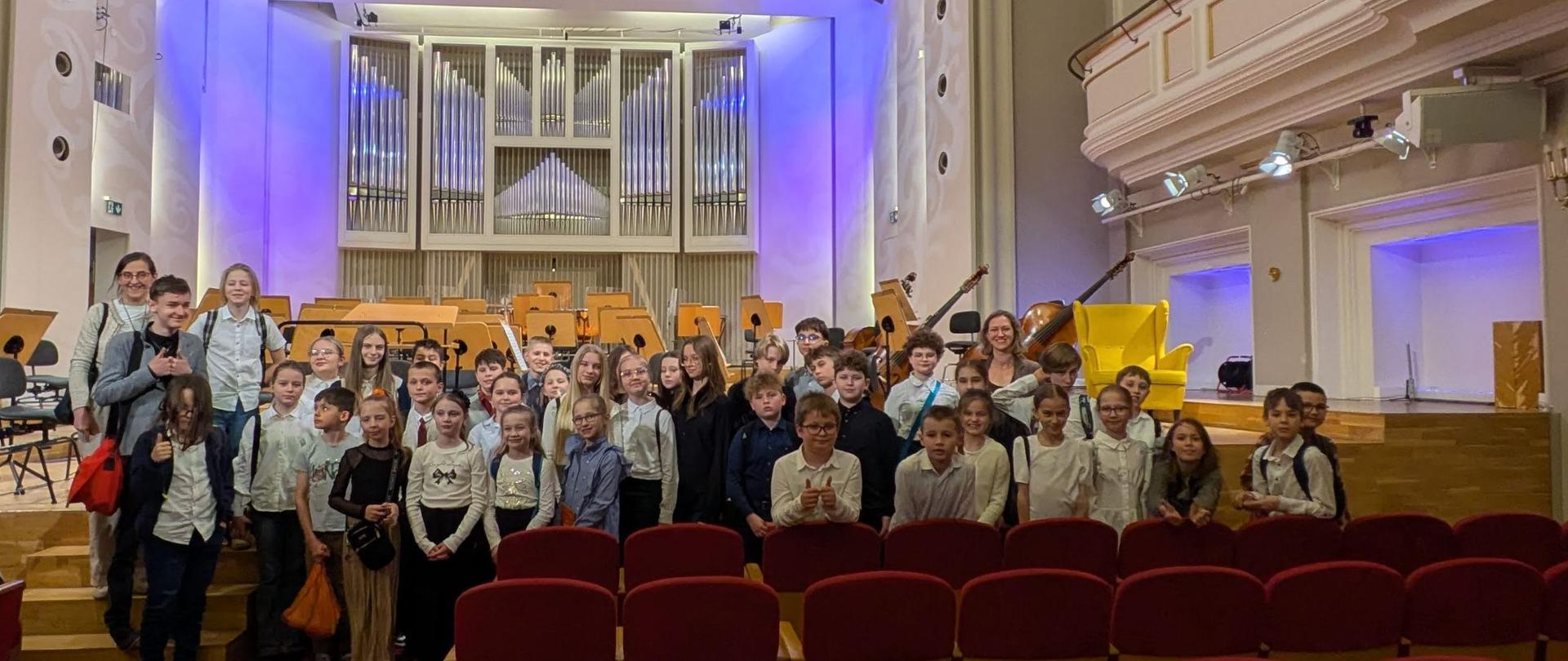 Wszyscy uczniowie biorący udział w wycieczce i nauczycielki stoją przed sceną Filharmonii.