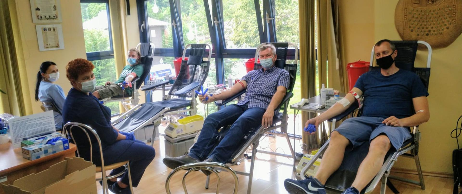 Trzy osoby siedzi na fotelach i oddaje krew.