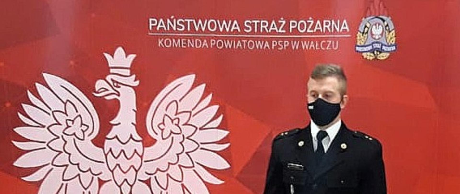 Zdjęcie przedstawia funkcjonariusza PSP na czerwony tle z białym orłem w koronie i logo PSP
