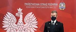 Zdjęcie przedstawia funkcjonariusza PSP na czerwony tle z białym orłem w koronie i logo PSP