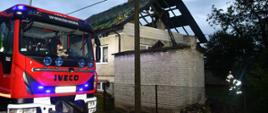 Na zdjęciu widzimy samochód strażacki, strażaków dokonujących rozpoznania w tle zniszczony budynek z zerwanym dachem.