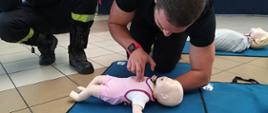 Zdjęcie przedstawia udzielanie przez strażaka kwalifikowanej pomocy przedmedyczne niemowlakowi.