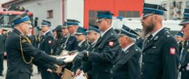 Na zdjęciu widoczny Świętokrzyski Komendant Wojewódzki w trakcie wręczania okolicznościowych dyplomów z okazji 30-lecia KSRG przedstawicielom poszczególnych jednostek OSP włączonych do KSRG. 