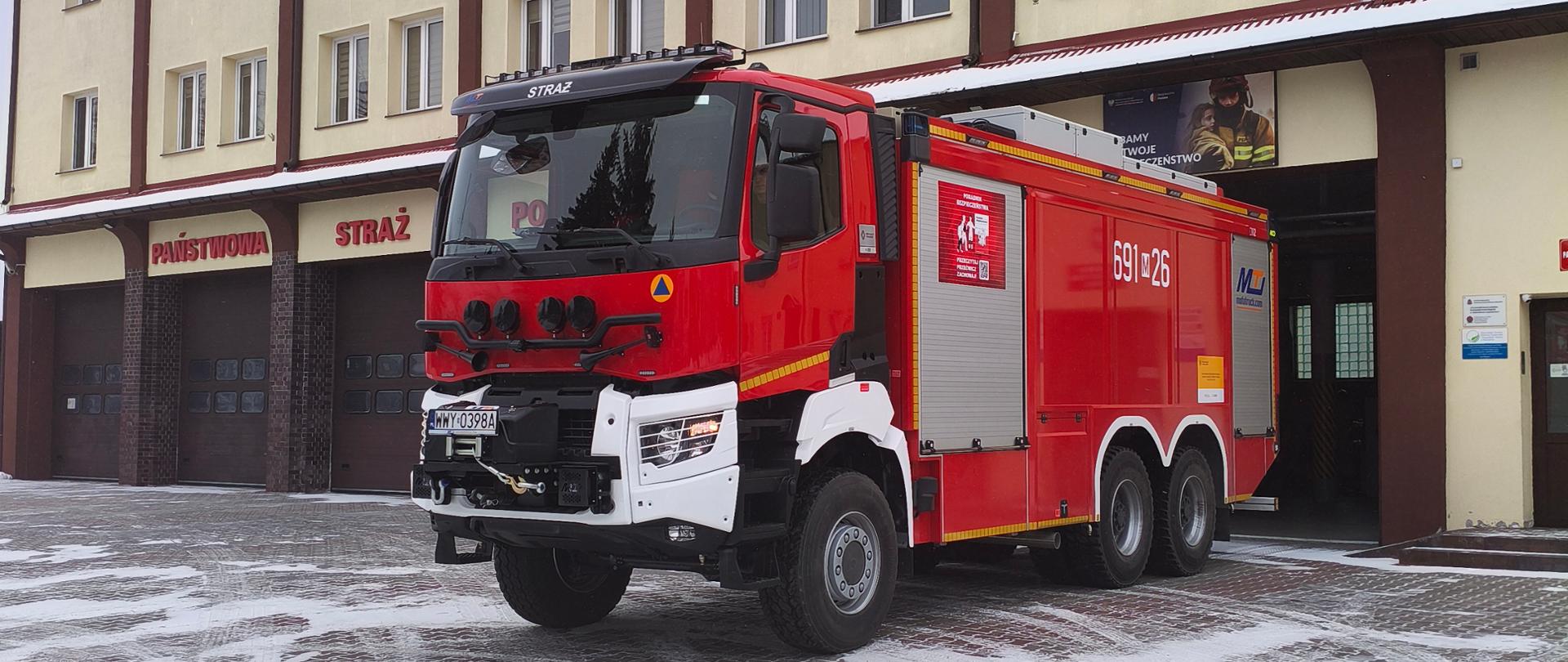 Samochód pożarniczy GCBA 10/65/5 Renault stoi przed budynkiem komendy.