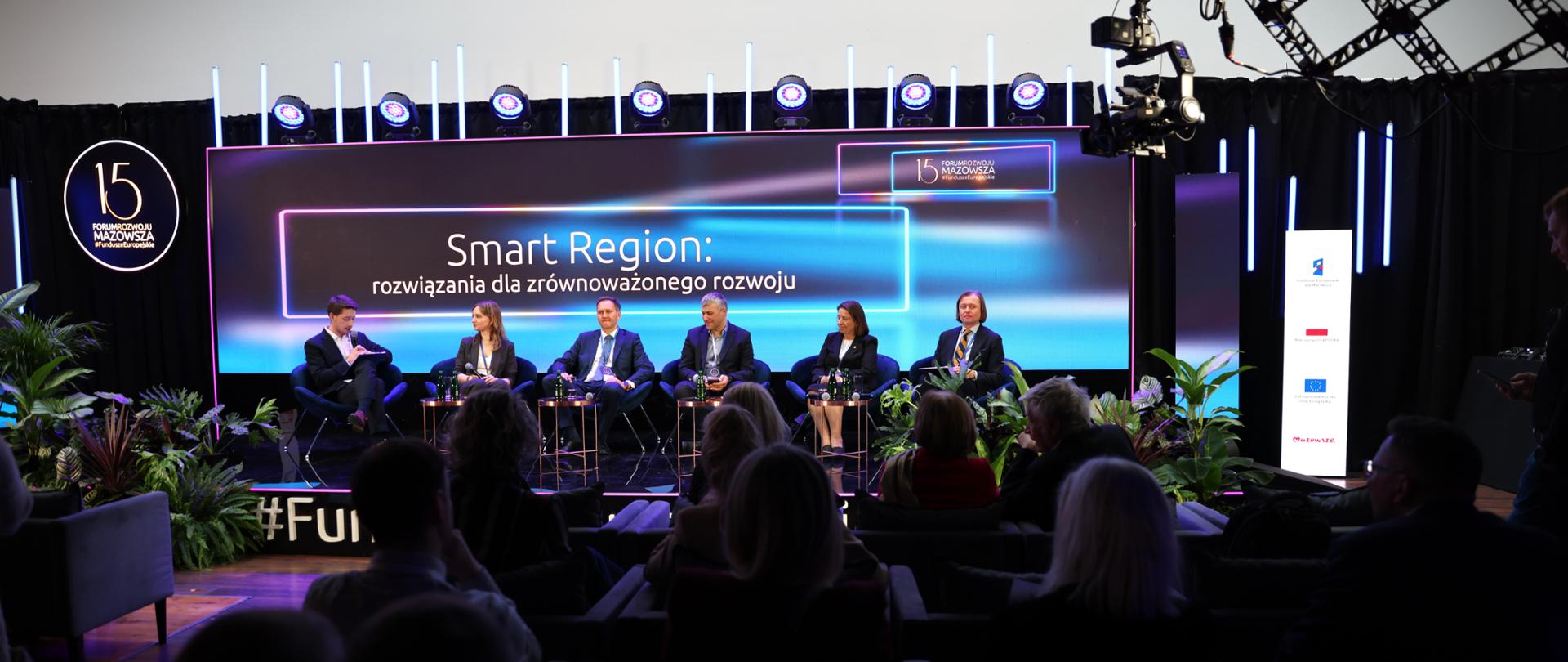 widok na sześć osób - uczestników jednego z paneli, z prawej wojewoda mazowiecki Mariusz Frankowski, w tle napis Smart Region: rozwiązania dla zrównoważonego rozwoju