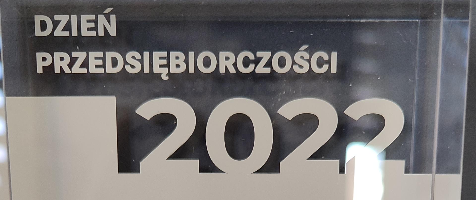 Szklana statuetka z napisem Dzień Przedsiębiorczości 2022 Najaktywniejsza instytucja, Patronat Honorowy Prezydenta Rzeczypospolitej Polskiej Andrzeja Dudy, Organizator: Fundacja Młodzieżowej Przedsiębiorczości.
