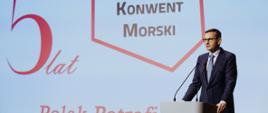 Premier Mateusz Morawiecki podczas wypowiedzi na Konwencie Morskim w Gdańsku. Szef rządu stoi przy mównicy z mikrofonami. W tle jest wyświetlana grafika: 5 lat Konwentu Morskiego z hasłem Polak Potrafi.